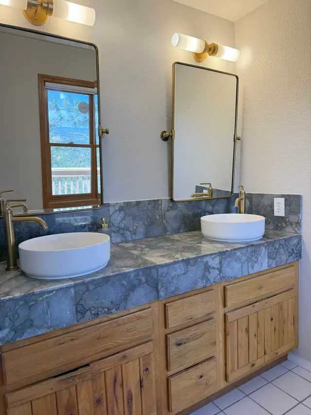 Vanity remodel with blue stone countertop, white vessel sinks, brass faucets and brass-framed mirrors