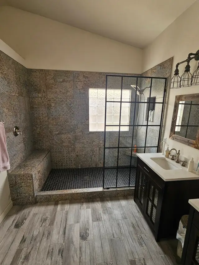 Full bathroom remodel with patterned stone-look wall tile, a black-framed glass shower, a built-in bench and a dark vanity