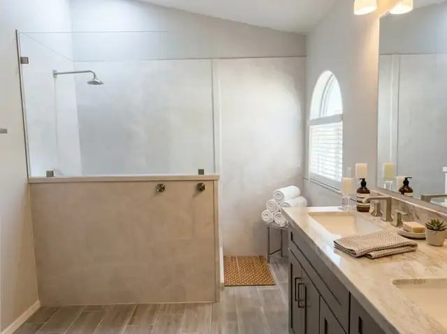 Primary bathroom with a glass-topped porcelain shower wall, a long dark vanity with a stone top and an arched window