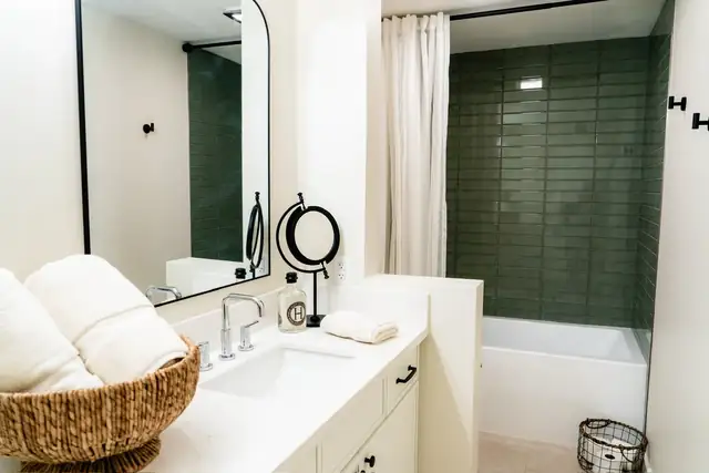 Guest bath with green glossy subway tile around the tub and a white vanity with round mirror