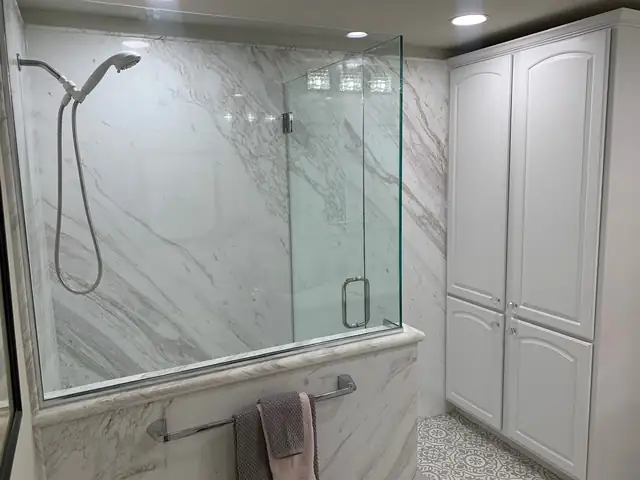 Porcelain slab shower in white and gray veining with a frameless glass panel, handheld shower and patterned tile floor