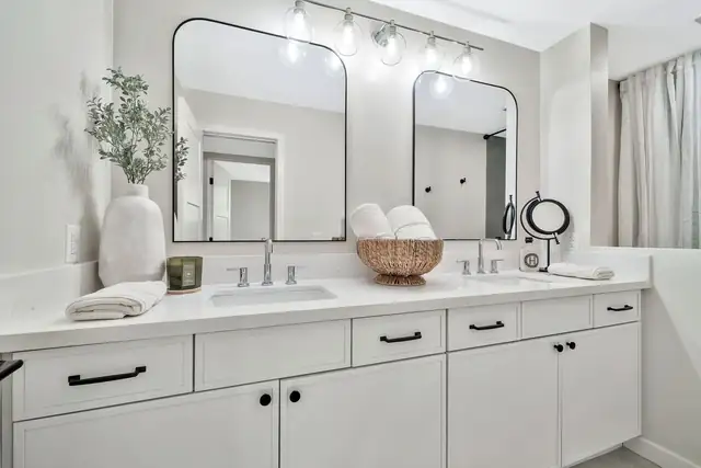 White double vanity with quartz top, black pulls, arched black mirrors and a vanity light bar