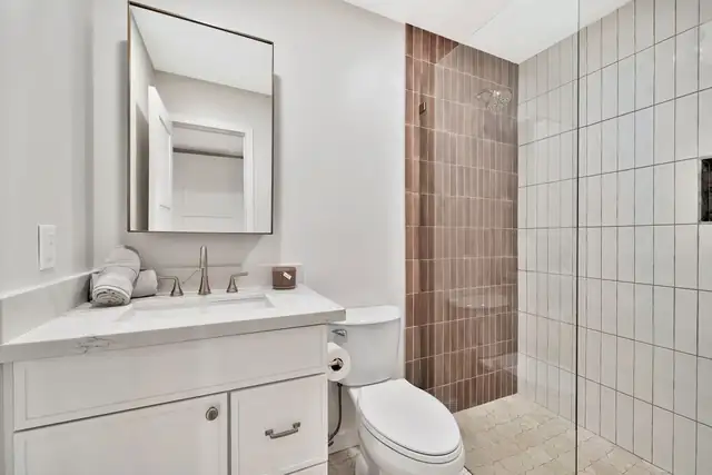 Guest bathroom with a white vanity, medicine cabinet and a walk-in shower with brown vertical tile accent