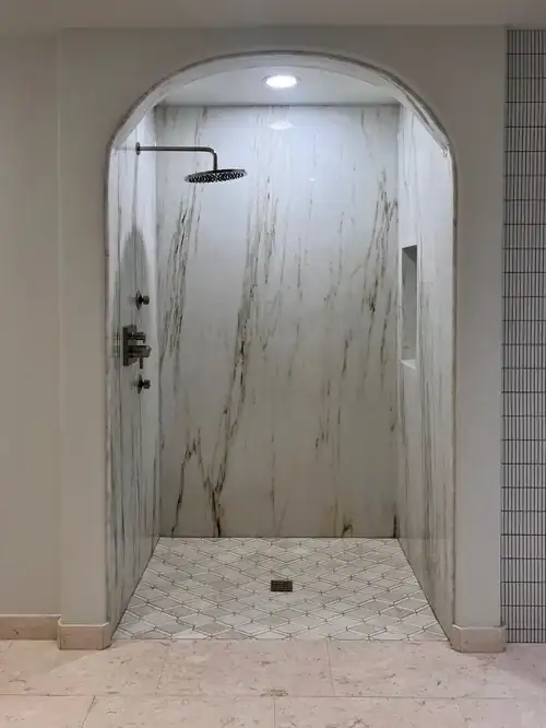Arched walk-in shower with veined porcelain slab walls, black rain head and recessed niche